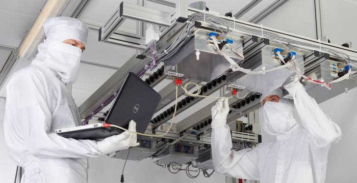 Two operators in cleanroom gowns maintaining industrial equipment