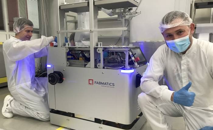 Two employees dressed in white in the clean room start up a mobile robot from Fabmatics.